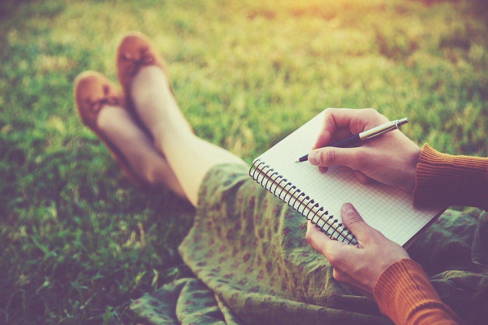 Woman Writing in Notebook on Grass