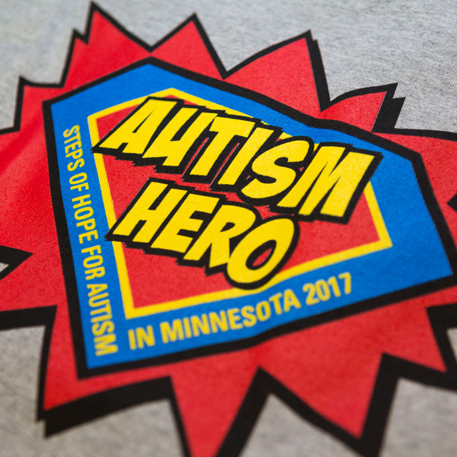 A super hero logo in the shape and color of the Superman logo with the words "Autism Her" in the center.