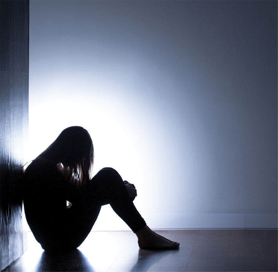 A darkened girl sitting in a room is holding her legs.