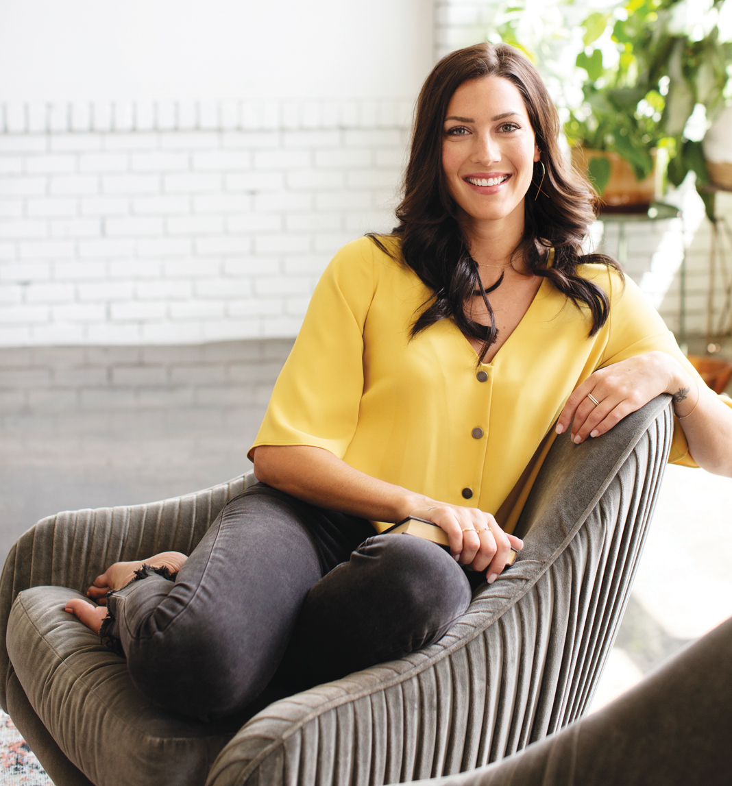 A portrait of Becca Kufrin sitting on a couch.