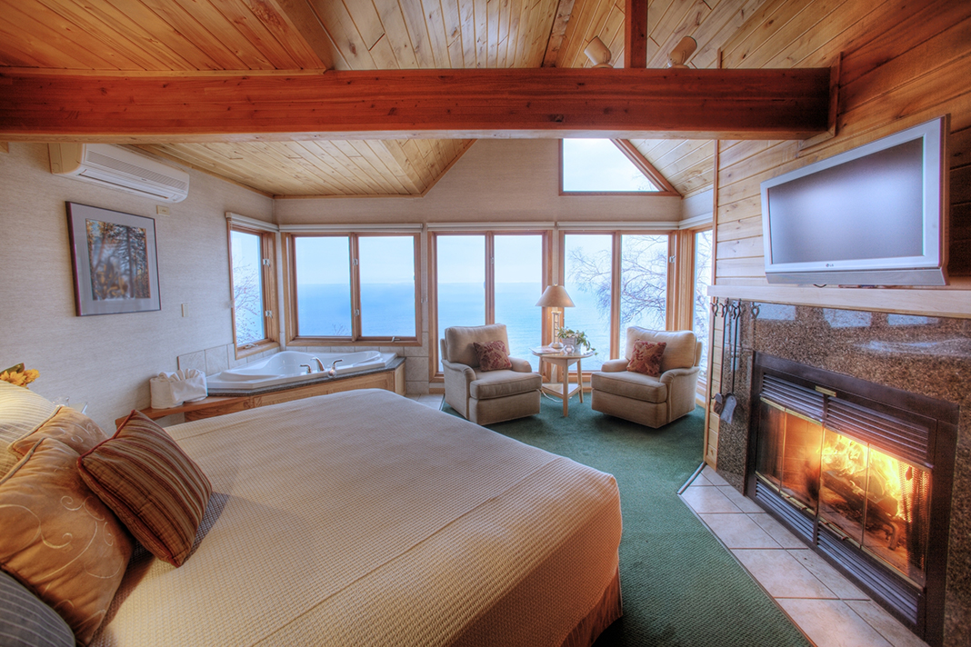 A lakeside resort room with green carpet, a queen-sized bed, jacuzzi tub, and fireplace. 