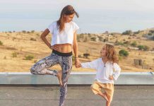mom and kid stand in a yoga pose on a mat