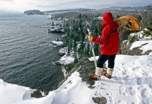 A woman carrying snowshoes looking over a snowy cliff