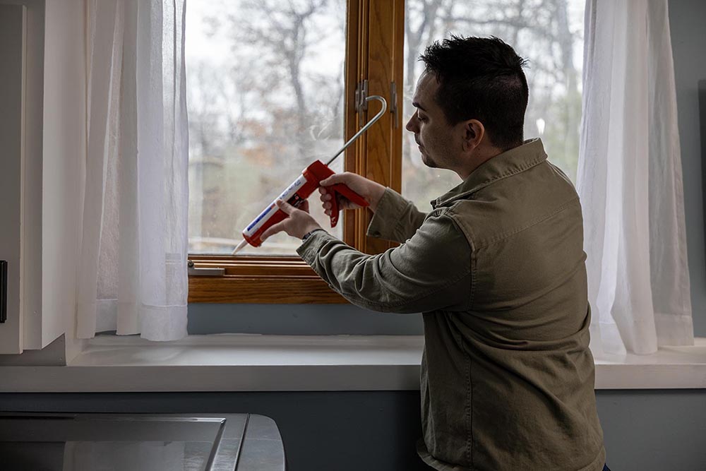 Man sealing window with Caulk